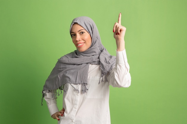 ヒジャーブの幸せなアラブの女性。緑のスタジオの背景でポーズをとって、笑顔の女の子の肖像画。