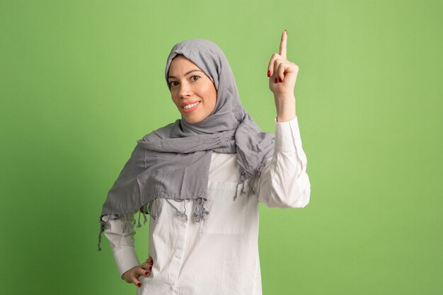 Счастливая арабская женщина в хиджабе. Портрет улыбающейся девушки, позирующей на зеленом фоне студии.