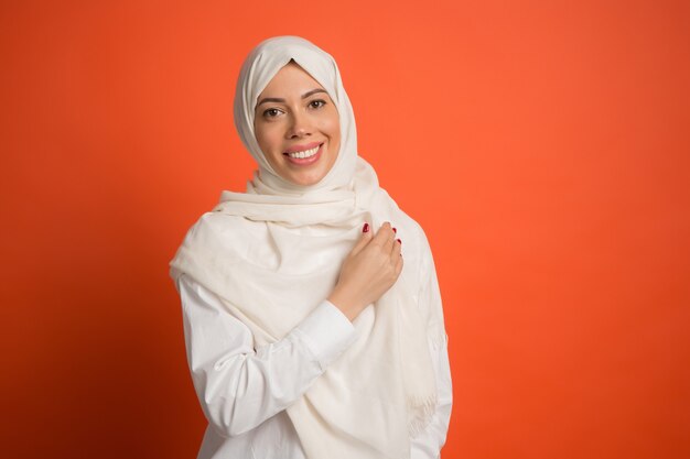 Hijab에서 행복 한 아랍 여자입니다. 빨간 스튜디오 배경에서 포즈 웃는 소녀의 초상화. 젊은 감정적 인 여자. 인간의 감정, 표정 개념. 전면보기.