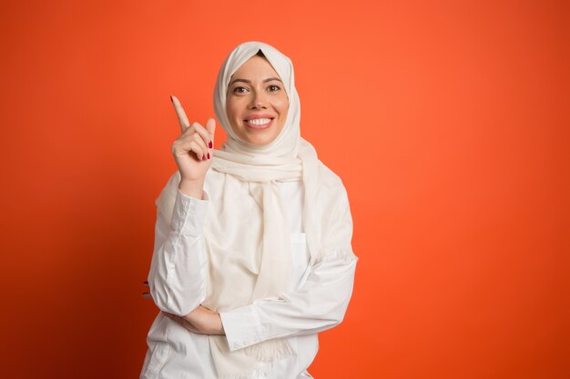 Счастливая арабская женщина в хиджабе. Портрет улыбающейся девушки, позирующей на красном фоне студии.