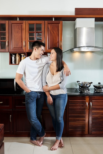 Happy Asian boyfriend and girlfriend hugging and looking at each other in kitchen