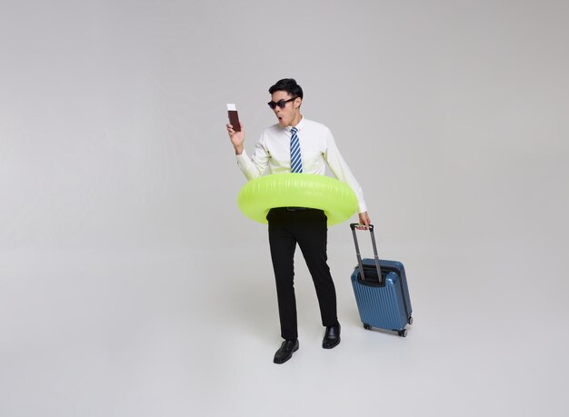 Happy asian business man holding inflatable swim ring and passport ticket walking with suitcase