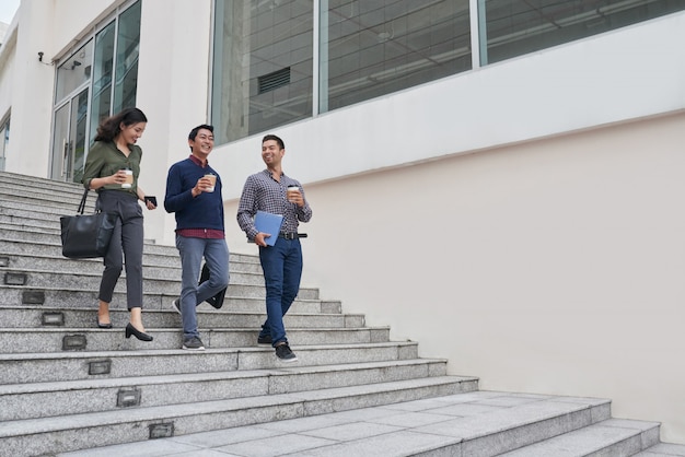 Happy Asian business people having coffee break leaving the office building for short promenade