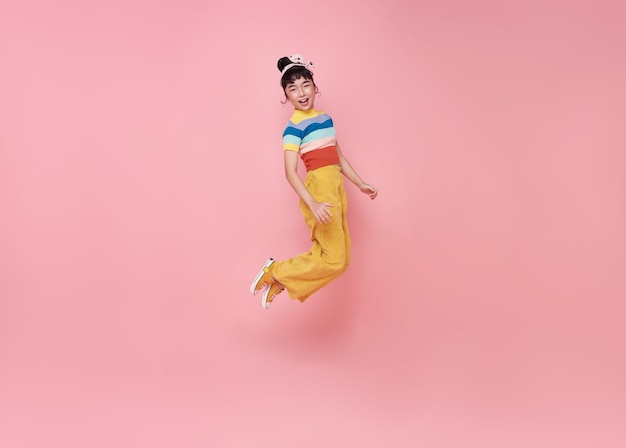 Счастливая азиатская девочка прыгает на розовом фоне