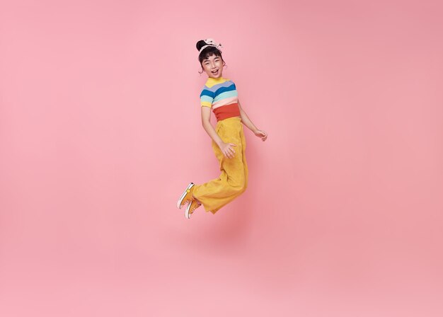 Счастливая азиатская девочка прыгает на розовом фоне