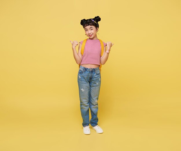 Счастливая азиатская девочка показывает пальцем вверх на желтом фоне с копировальным пространством