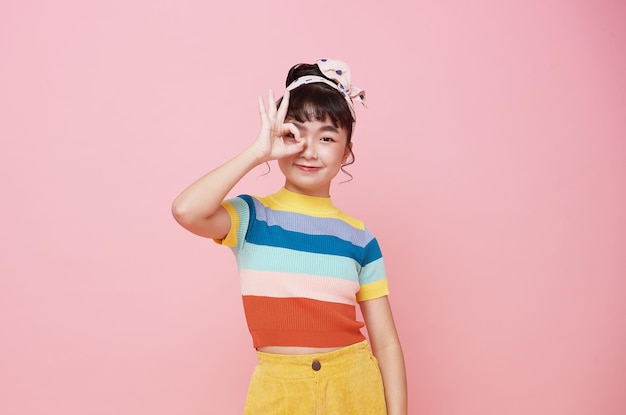 Happy Asian child girl showing hand ok isolated on pink background