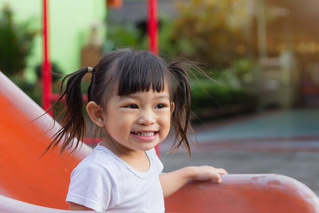 幸せなアジアの子供の女の子の笑顔と布のマスクを身に着けています 彼女は遊び場でスライダーバーのおもちゃで遊んでいます プレミアム写真 幸せなアジアの子供の女の子の笑顔と布のマスクを身に着けています 彼女は遊び場でスライダーバーのおもちゃで遊んでいます プレミアム写真