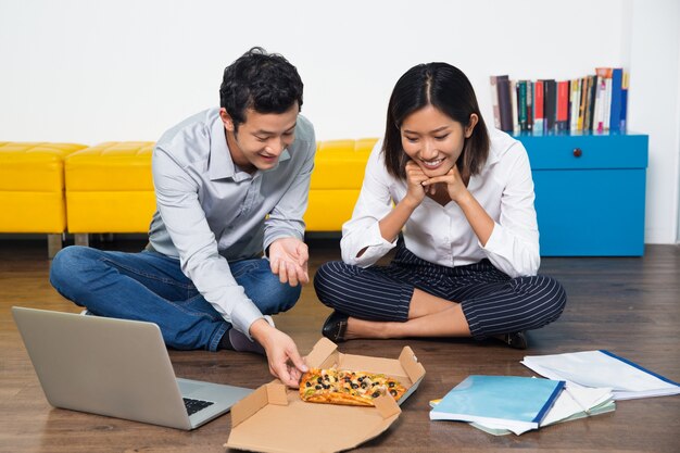 Happy Asian colleagues eating pizza on floor