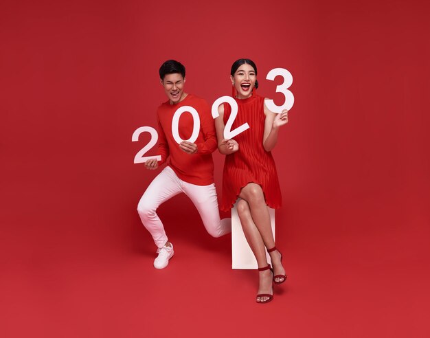 Счастливая азиатская пара в красной повседневной одежде с номером 2023 поздравляет с новым годом