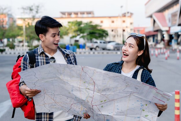 紙の地図を持って旅行中に方向を探している幸せなアジアのカップルの観光バックパッカー、彼らは紙の地図の目的地の場所に到着したときに喜んで笑います。