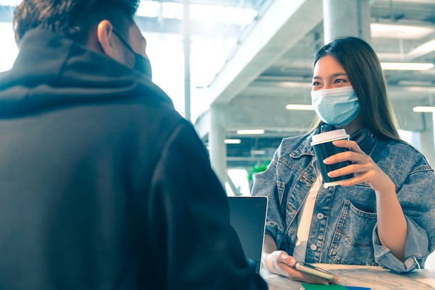 Happy asian couple wear face mask virus protection in a coffee shop enjoy good conversation Young man and woman in a restaurant looking at touch screen computer laugh smile together