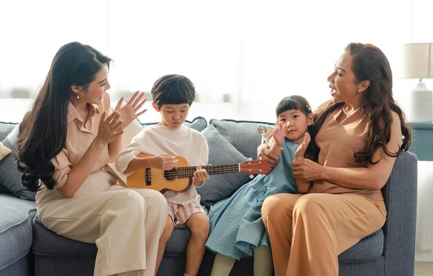 Happy Asian family grandchild with grandmother playing guitar and singing a song together at home