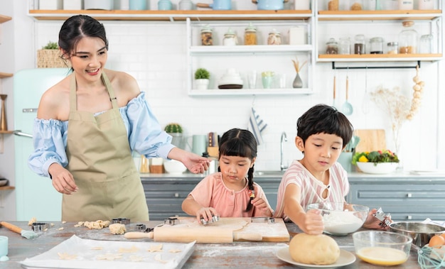 행복한 아시아 가족이 준비 반죽을 만들고 집에서 부엌에서 쿠키를 굽습니다.