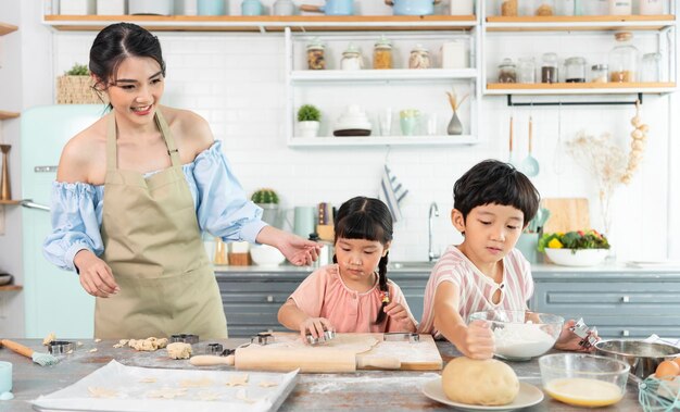 幸せなアジアの家族が準備生地を作り、自宅のキッチンでクッキーを焼く家族をお楽しみください