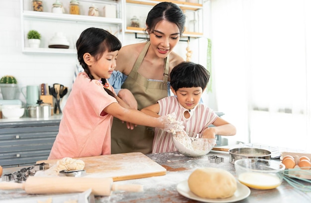 幸せなアジアの家族が準備生地を作り、自宅のキッチンでクッキーを焼く家族をお楽しみください