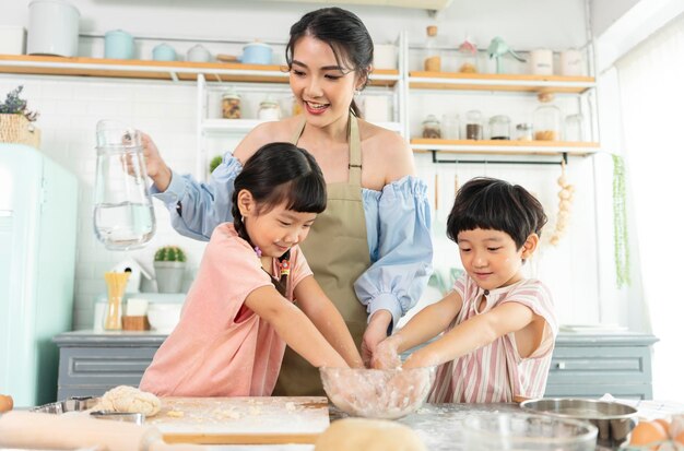 幸せなアジアの家族が準備生地を作り、自宅のキッチンでクッキーを焼く家族をお楽しみください