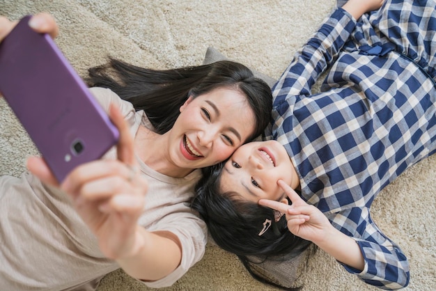 Happy Asian Family mother and daughter making a selfie photo while use in living room home background