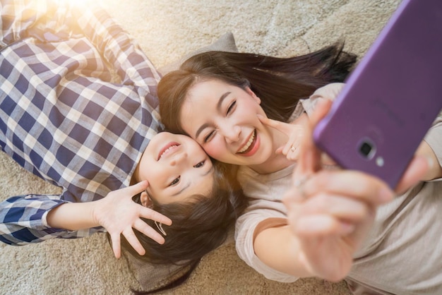 Happy Asian Family mother and daughter making a selfie photo while use in living room home background