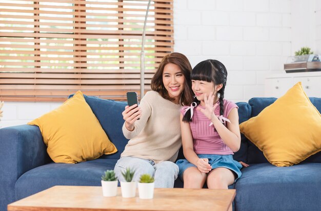 スマートフォンを使って、自宅のリビング ルームのソファで一緒に自撮り写真を撮る幸せなアジアの家族。