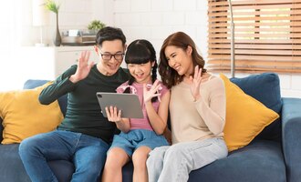 Happy asian family using tablet video call virtual meeting together on sofa at home living room