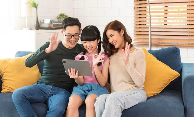 가정 거실 소파에서 태블릿 화상 통화 가상 회의를 사용하는 행복한 아시아 가족