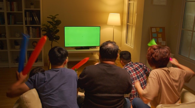 Счастливые азиатские друзья или футбольные фанаты смотрят футбол на экране Green Chroma Key