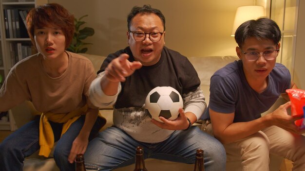 幸せなアジアの友人やフットボールのファンがテレビでサッカーを見て、家で勝利を祝う友情スポーツとエンターテイメントのコンセプト