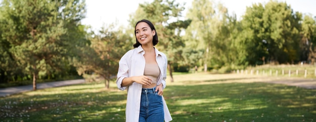 Free photo happy asian girl dancing in park feeling freedom and joy walking outdoors on sunny day