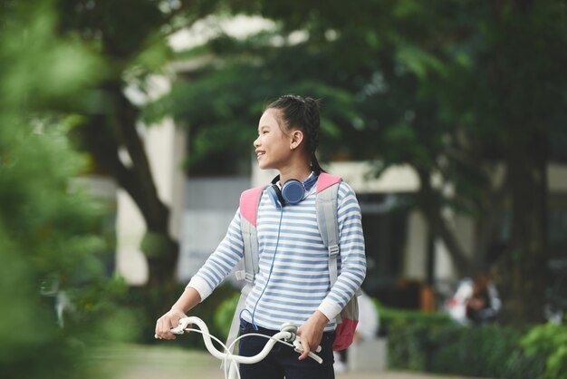 Happy Asian girl holding bicycle and looking around in park