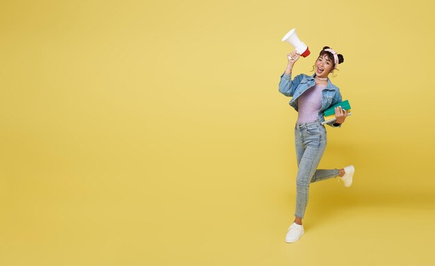 Счастливая азиатская девушка держит книгу и прыгает, крича на мегафон объявления
