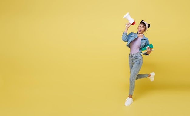 행복한 아시아 소녀가 책을 들고 발표 확성기에 소리를 지르며 뛰어오르고 있다