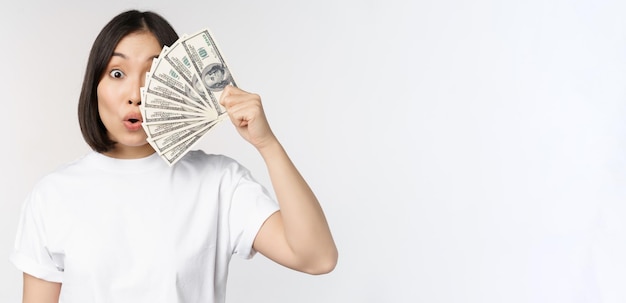 Free photo happy asian girl holding money cash near face concept of microcredit and finance white studio background copy space