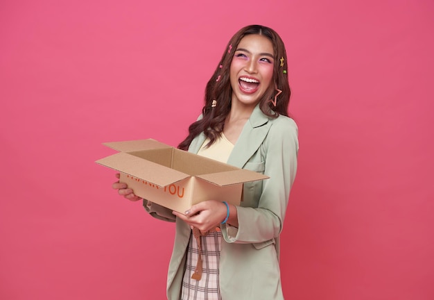Счастливая азиатская девушка держит открытую коробку с посылкой на розовом фоне