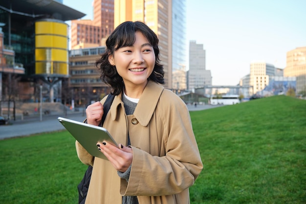 행복 한 아시아 소녀는 거리 대학생 손에 디지털 태블릿과 미소 s 산책에 서