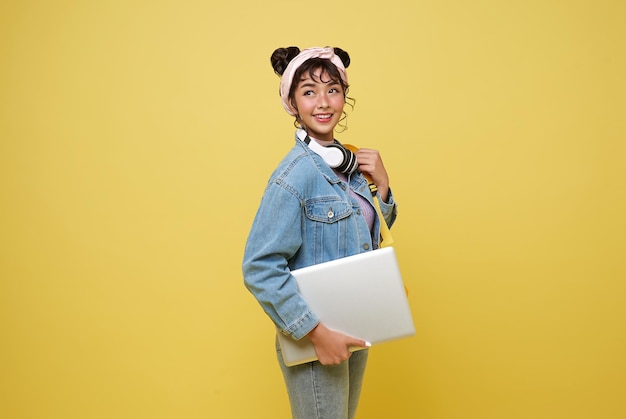 Foto gratuita studente asiatica felice con laptop e zaino isolata sullo sfondo giallo dello studio