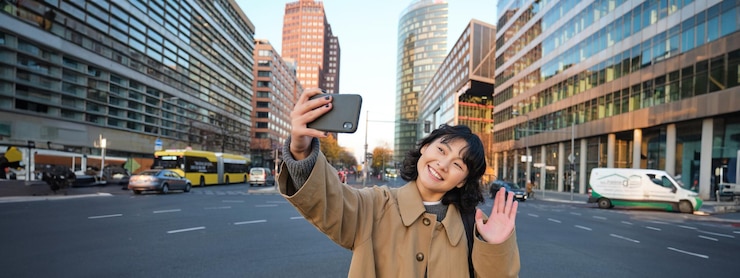 無料Photo 幸せなアジアの女の子観光客が市内中心部で自撮りをし、ビデオ通話をし、スマートフォンのカメラに手を振る
