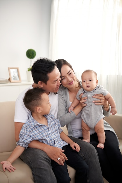 Happy Asian husband, wife and two kids sitting on couch at home