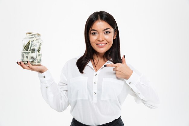 親指を現してお金で瓶を保持している幸せなアジアの女性。