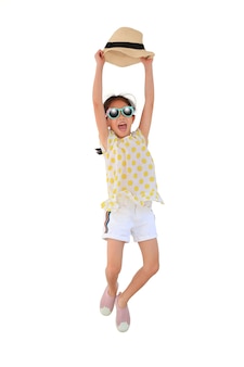 선글라스를 끼고 흰색 외진 배경에서 점프하는 밀짚 모자를 들어 올리는 행복한 아시아 소녀. 여름과 패션 컨셉