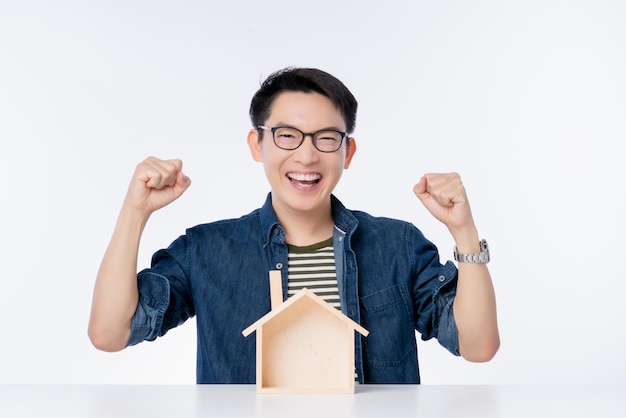 Free photo happy asian male casual lifestyle smile laugh hand rise up with house model on table exiting asian man with big success promotion business ideas concept