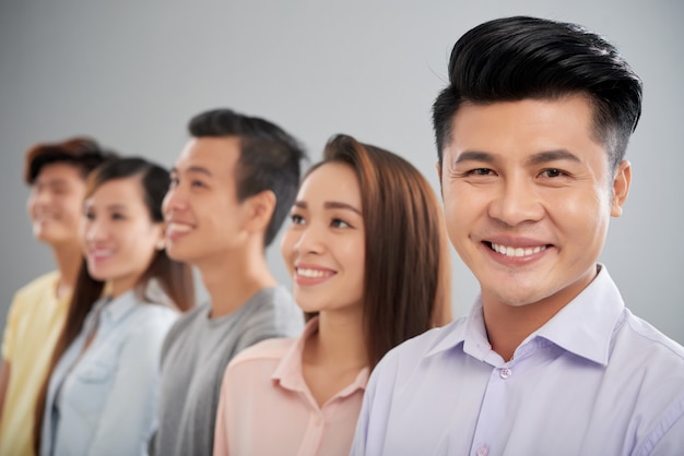 Happy Asian man looking at camera standing in the foreground of his colleagues