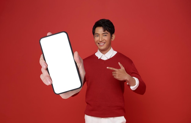 Happy Asian man wearing red dress showing mobile phone and pointing finger at blank screen