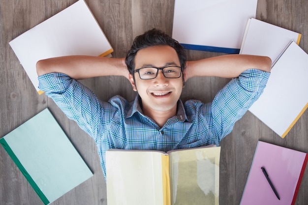 Free photo happy asian student boy lying on floor among books