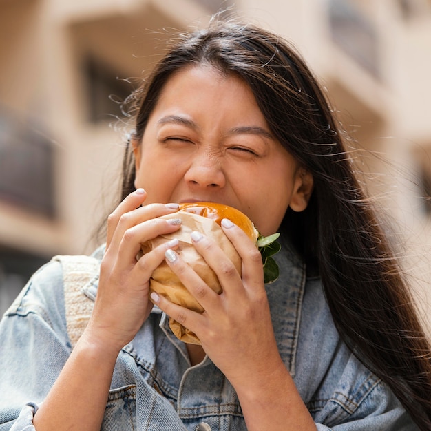 Happy asian woman eating a burger outdoors