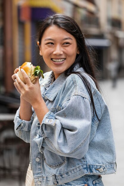 Happy asian woman eating a burger outdoors