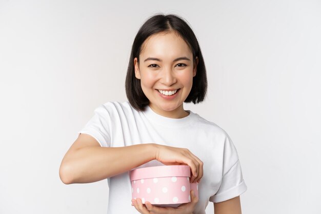 Happy asian woman girlfriend open box with valentines day gift receive romantic present standing over white background