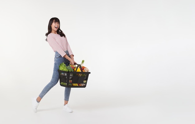 Happy Asian woman holding shopping basket full of vegetables and groceries studio shot