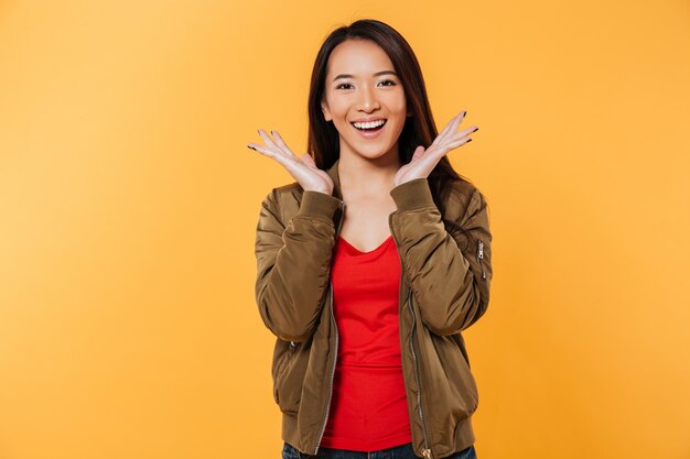 Happy asian woman in jacket holding hands near head