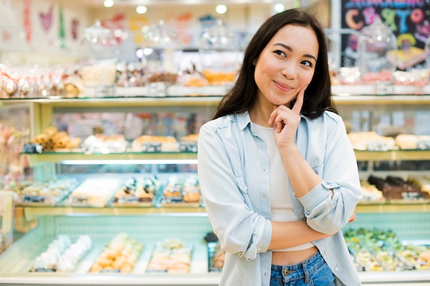 Счастливая азиатская женщина выбирая десерт в магазине хлебопекарни